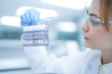 Focused female scientist holding a rack of glass slides for microscopic analysis in a sterile clinical laboratory. Professional medical researcher examining tissue samples for diagnosis.