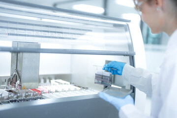 Focused female scientist loading a rack of microscope slides into an automated staining machine in a sterile laboratory. Professional researcher preparing tissue samples for pathology diagnosis.