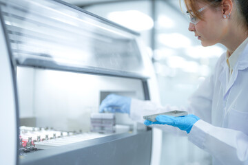Medical researcher operating digital analyzer interface in sterile laboratory. Specialist holding biological samples in rack while setting calibration for pharmaceutical testing.