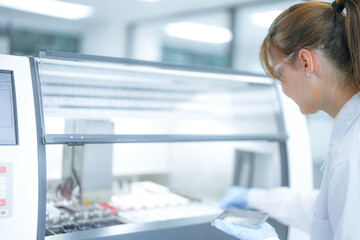 Focused female scientist loading a rack of microscope slides into an automated staining machine in a sterile laboratory. Professional researcher preparing tissue samples for pathology diagnosis.