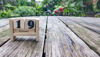 wooden cube calendar for January 19th place on old table in sunny garden background