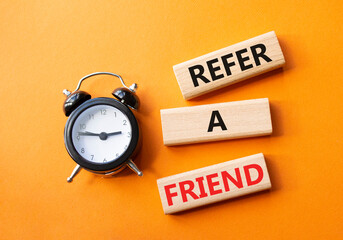 Refer a Friend symbol. Concept words Refer a Friend on wooden blocks. Beautiful orange background with alarm clock. Business and Refer a Friend concept. Copy space.