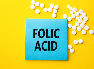 Folic acid symbol. Concept word Folic acid on blue note. Beautiful yellow background with pills. Medicine and Folic acid concept. Copy space