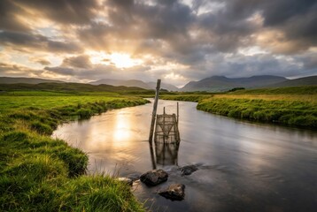 Peaceful river landscape at sunrise, wooden fish trap in stream, green meadow banks, dramatic cloudy sky, reflections, tranquil nature scenery in mountain valley
