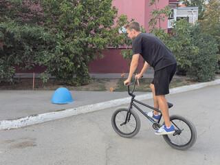 Obraz premium A person rides a BMX bike on a street while trees surround the area and a blue object is nearby