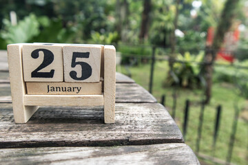 wooden cube calendar for January 25th place on old table in sunny garden background