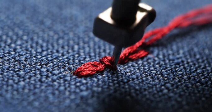 Close-up of a needle stitching red thread onto blue fabric, showcasing intricate embroidery techniques