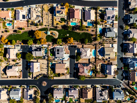 Top-down aerial view of suburban houses with private swimming pools and intersecting streets in a planned desert neighborhood