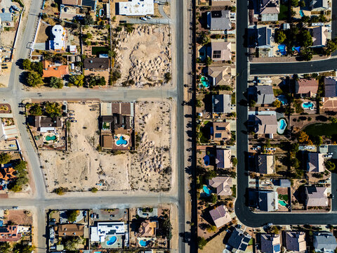 Aerial view of suburban residential neighborhood in Los Angeles desert area with intersecting streets, detached houses, swimming pools, dry landscapes, and low density urban planning seen from directl