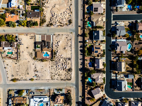 Aerial view of suburban residential neighborhood in Los Angeles desert area with intersecting streets, detached houses, swimming pools, dry landscapes, and low density urban planning seen from directl