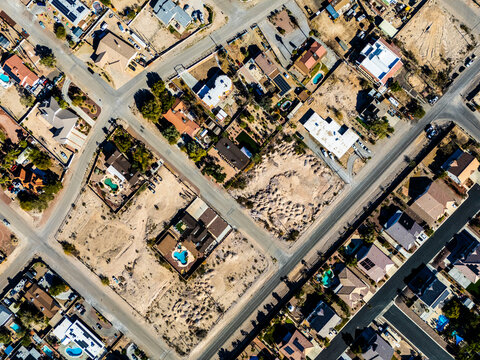 Aerial view of suburban residential neighborhood in Los Angeles desert area with intersecting streets, detached houses, swimming pools, dry landscapes, and low density urban planning seen from directl