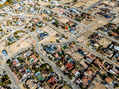 Aerial view of suburban residential neighborhood in Los Angeles desert area with intersecting streets, detached houses, swimming pools, dry landscapes, and low density urban planning seen from directl