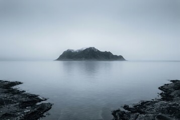 Rocky island in misty sea seascape, calm water and foggy horizon, framed by dark rocks, minimalist moody coastal landscape, solitude and tranquility concept
