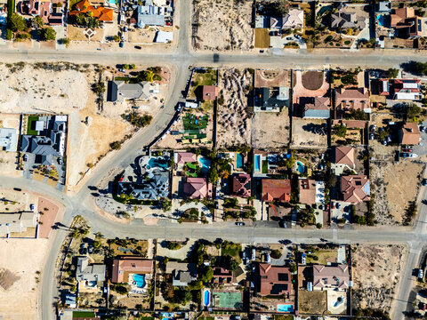 Aerial view of suburban residential neighborhood in Los Angeles desert area with intersecting streets, detached houses, swimming pools, dry landscapes, and low density urban planning seen from directl