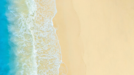 Aerial video shows waves crashing against a tropical coastline with turquoise, clear waters contrasting with a bright sky, and coral reefs on the shores of a tropical island with emerald waters.