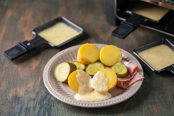 Delicious traditional Swiss melted raclette cheese on diced boiled or baked vegetables served in individual skillets