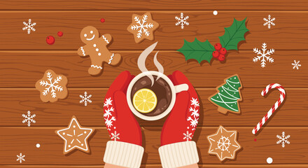 Top view of hands wearing red mittens holding a hot chocolate cup with lemon surrounded by gingerbread cookies on a wooden table surface.