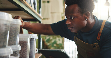 Fototapeta premium Black man, tablet and stock in nursery with checklist, inventory management or online order. Entrepreneur, sustainable business and tech at shelf for compost storage, soil quantity or quality control