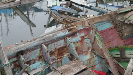 Fototapeta premium Fishing boats made of wood are damaged and not repaired, plus there is a scattering of plastic waste around the estuary. Beaches like this make the environment smelly and the fish become unhealthy