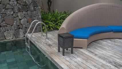 Swimming pool. A fragment. A metal ladder descends into the clear turquoise water. Tiled bottom. There is a rattan sofa with soft cushions on the wooden terrace. Mauritius. Resort. Hotel.