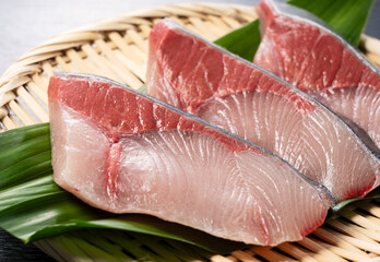 Fresh Japanese Yellowtail Fillets on Bamboo Tray with Green Leaves.
