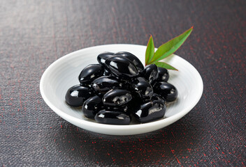 Traditional Japanese New Year Dish: Glossy Sweetened Black Soybeans (Kuromame) on a White Plate with Copy Space