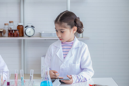 Cheerful Arabian girl primary school student wearing lab coats studying research attention to chemical substance analyzing in microscope in laboratory room, lifestyle learning education science class - Powered by Adobe