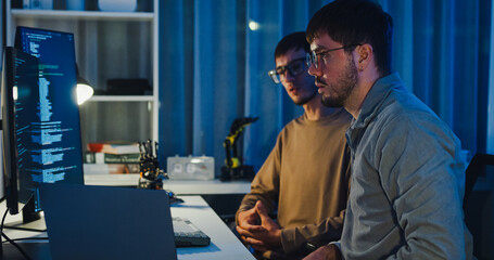 Team adult male engineer collaborate on robotic hand project using AI code solutions machine learning at tech workspace night. Artificial intelligence interface, collaboration prototype development.