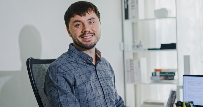 Portrait confident smiling male programmer working with robotics code AI software and looking at camera in tech office. Artificial intelligence dashboard, robotics, user interface, machine learning.