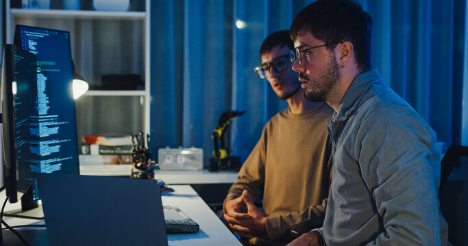 Team adult male engineer collaborate on robotic hand project using AI code solutions machine learning at tech workspace night. Artificial intelligence interface, collaboration prototype development.