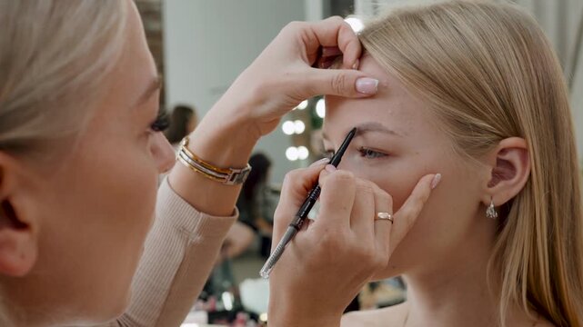 The makeup artist paints the eyebrows of the model with a special brush along the contour. Professional makeup close up.