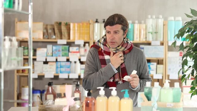 Adult man buyer with sore throat and cough choosing medicines and hygiene products in pharmacy
