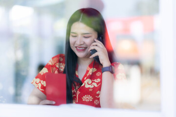 Portrait of asian woman wearing red cheongsam dress holding red envelopes and smartphone at home in the living room indoor decoration for Chinese new year festival celebrate culture of china holiday