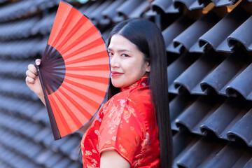 Portrait beautiful smiles Asian young woman wearing red traditional Chinese decoration and holding a Chinese Fanning  for Chinese New Year Festival at Chinese restaurant cafe.