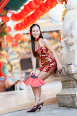 Portrait beautiful smiles Asian young woman wearing red traditional Chinese cheongsam decoration and holding a Chinese Fanning for Chinese New Year Festival at Chinese shrine in Thailand