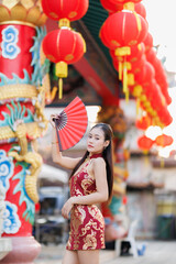 Portrait beautiful smiles Asian young woman wearing red traditional Chinese cheongsam decoration and holding a Chinese Fanning for Chinese New Year Festival at Chinese shrine in Thailand
