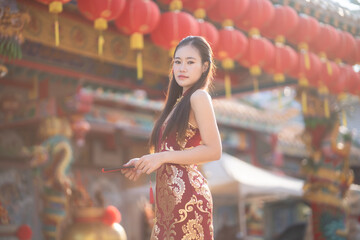 Portrait beautiful smiles Asian young woman wearing red traditional Chinese cheongsam decoration and holding a Chinese Fanning for Chinese New Year Festival at Chinese shrine in Thailand