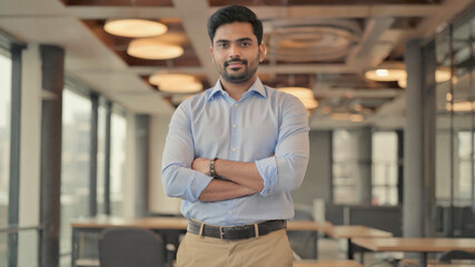Young man in stylish casual clothes standing in front of shelves inside office.