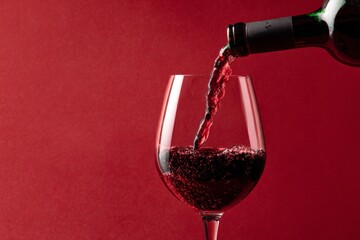 red wine pouring from a bottle into a glass against a red background