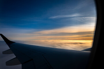 Airplane wing flying over golden clouds at sunset seen through the window