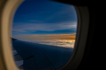 Airplane wing flying over golden clouds at sunset seen through the window