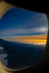 Airplane wing flying over golden clouds at sunset seen through the window