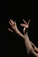 Two expressive female hands with red nails reach upward in a delicate, artistic gesture against a black background, emphasizing contrast and form
