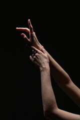 Female hands in an elegant, expressive gesture with soft lighting against a black background. Emphasizes form, texture, and emotion
