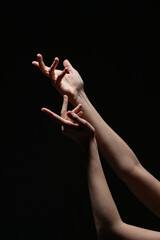 Two feminine hands caught in a dynamic, graceful motion with soft lighting against a black background. Evokes emotion and elegance in a minimalist style