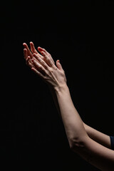 Close-up of two female hands with red nails in an expressive, illuminated pose against a dark backdrop. A minimal, artistic composition