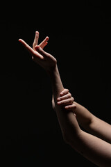 Female hands in a poised, expressive gesture illuminated against a black background. Graceful and emotive composition with minimal lighting