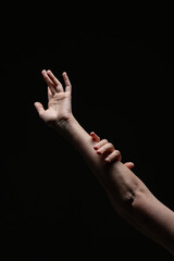 A single hand extended upward in a graceful gesture, lit against a black background with subtle highlights on skin and nails. Minimalist and expressive