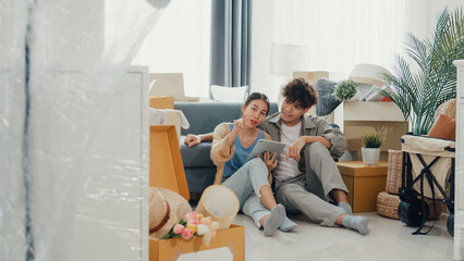 Young happy Asia couple sit on sofa couch use digital tablet online shopping furniture from decoration store in living room at home. Husband wife move new house, Apartment Rent And Ownership Concept.