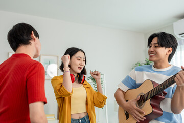 Diverse Asian friends playing guitar and dancing in living room at home.